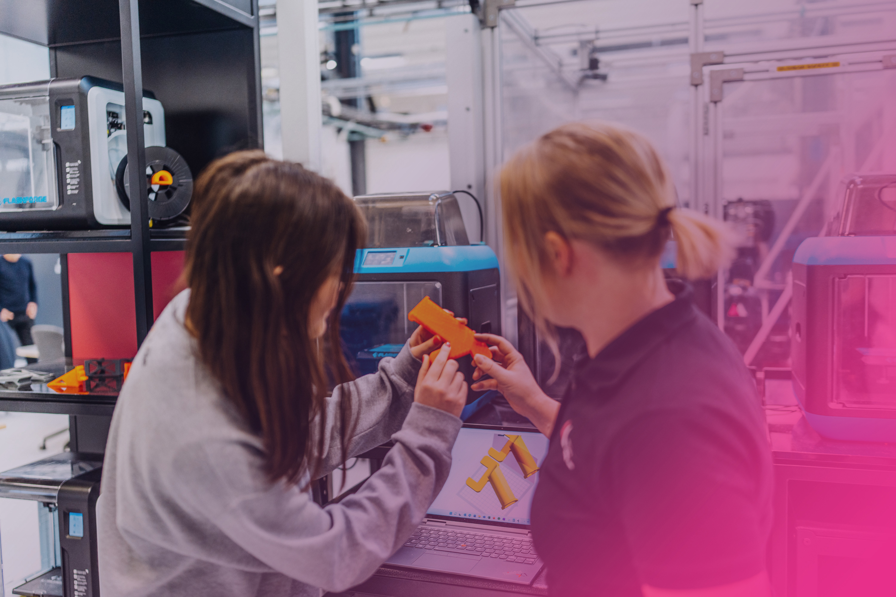 A young woman is being tutored by her female supervisor at a machine with a screen.