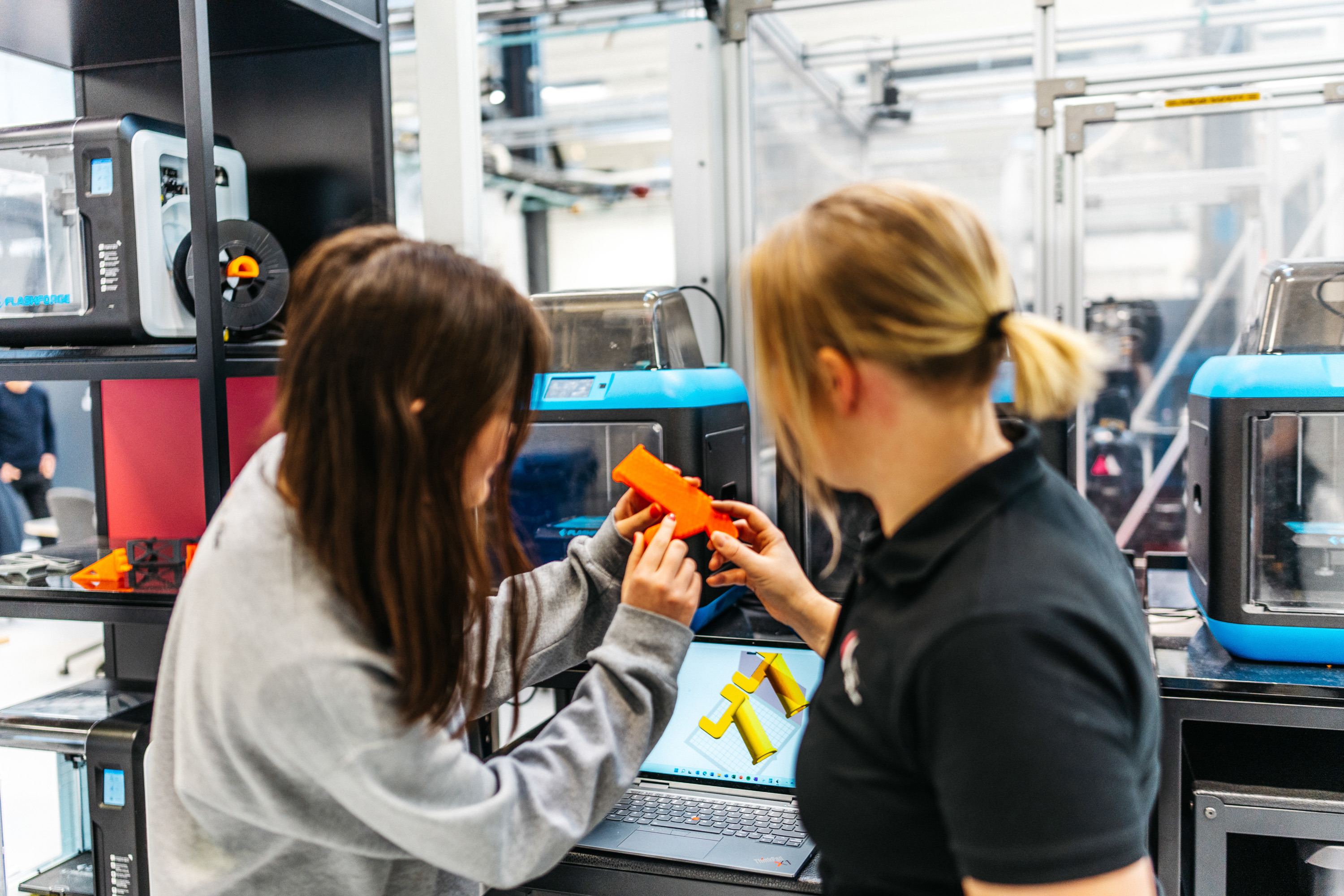 En ung kvinna får handledning av sin kvinnliga handledare vid en maskin med skärm. 