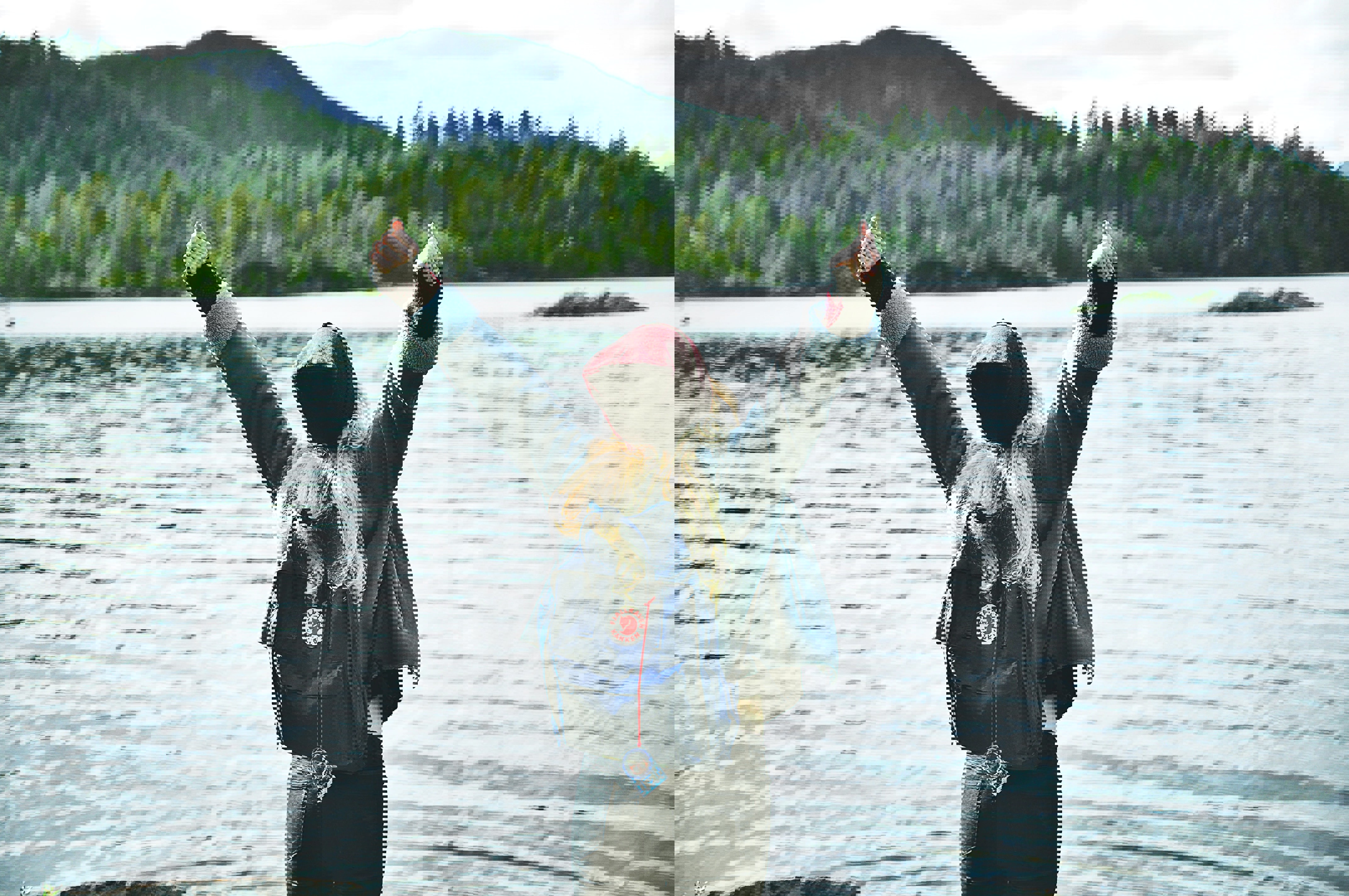 Kvinna framför en stor sjö, med en fjällräven ryggsäck på ryggen, sträcker upp armarna 