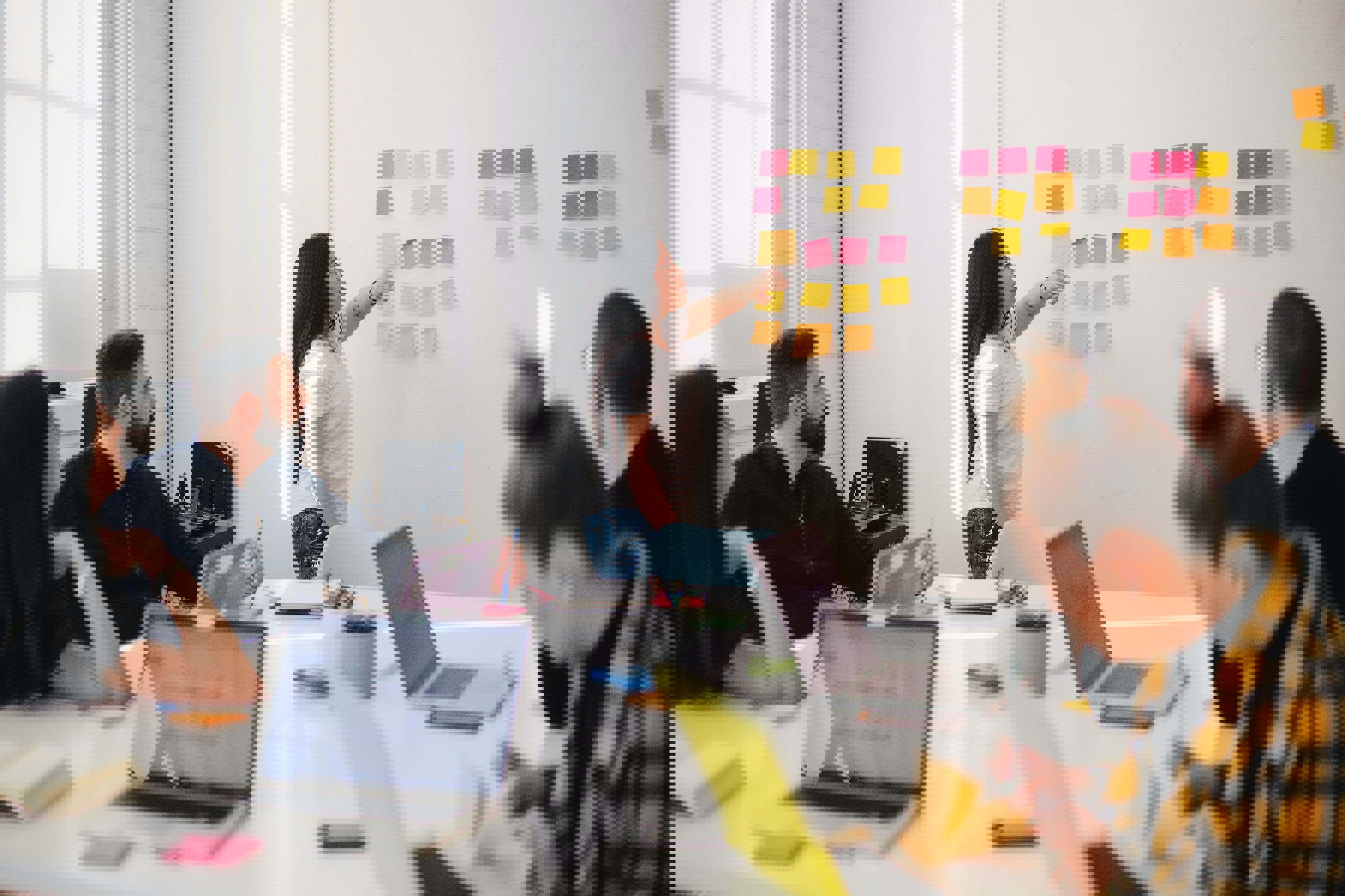 Kvinna vid whiteboard täckt i postitlappar presenterar för en grupp personer 