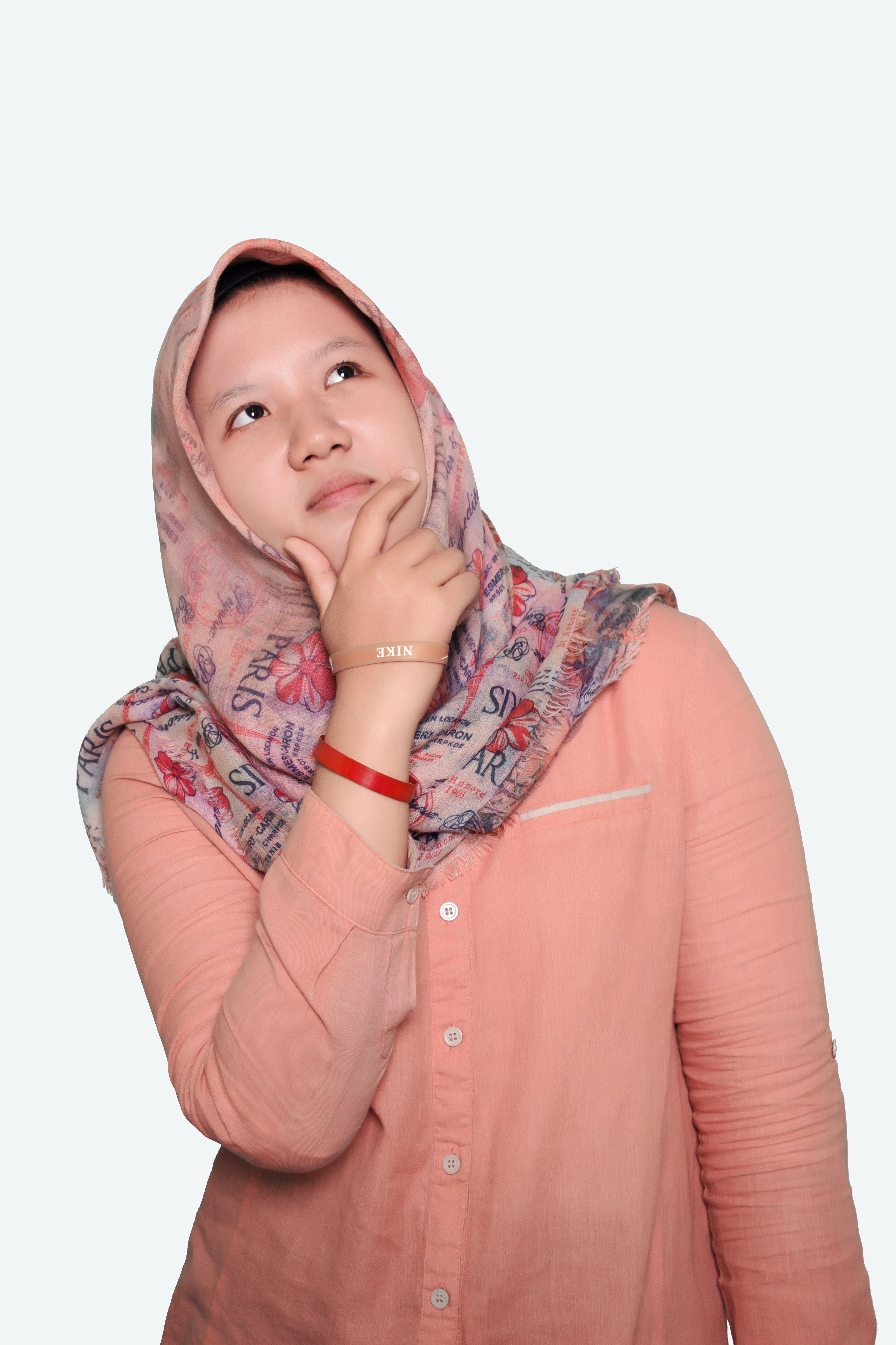 A woman in a hijab is thinking about something, with one hand on her face, her head tilted and her eyes fixed upwards.